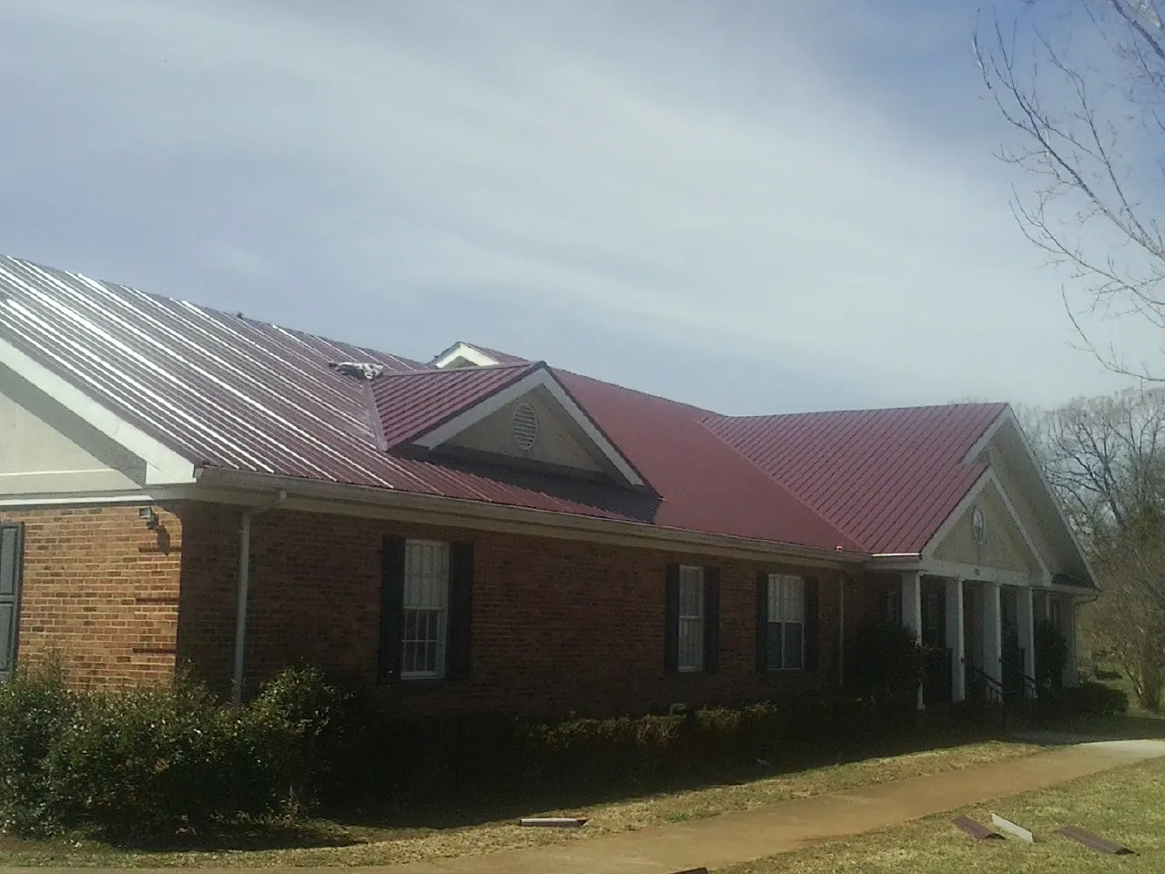 Red metal roof with gabled entries on a long brick building, from a Hail Damage Roof Repair job in East Orange