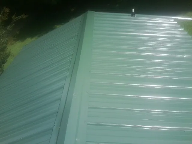 New green metal panels meeting at the ridge of a roof — Flat Roof Repair work by our crew in East Orange