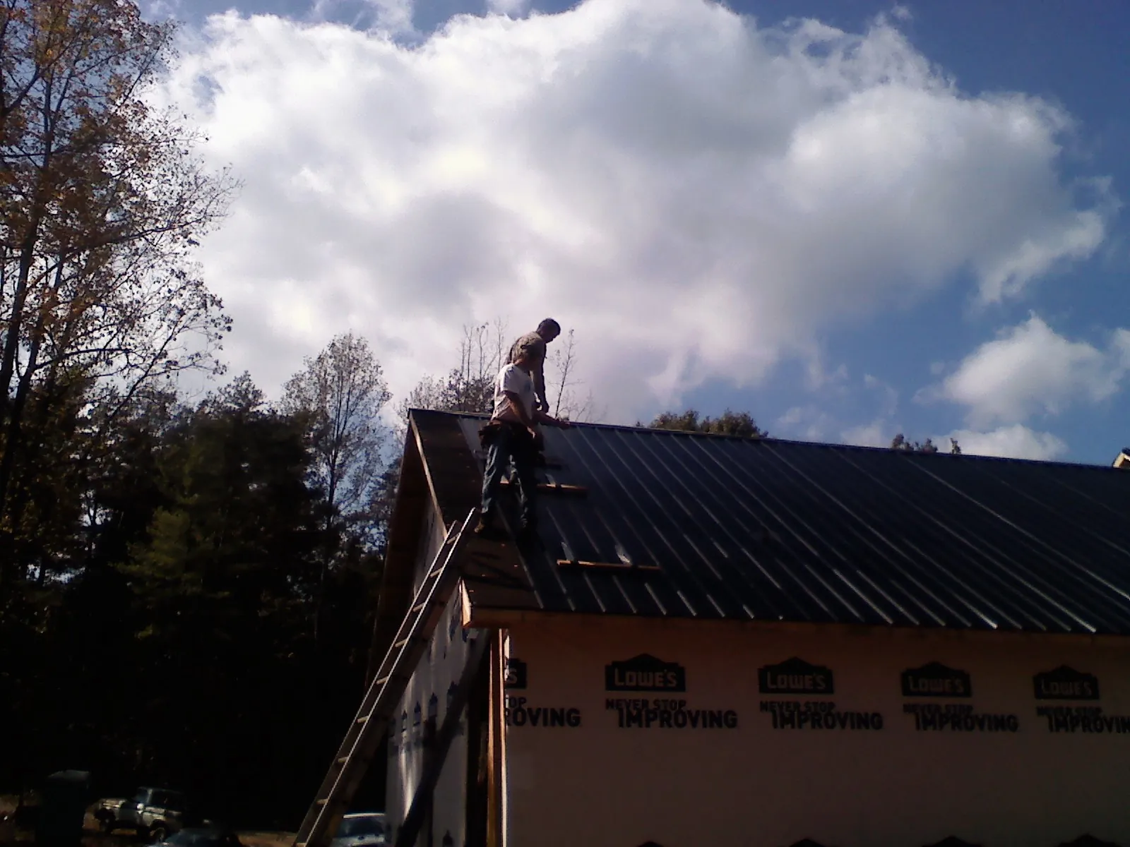 Roofer fastening dark metal panels high against a cloudy sky, from a Roof Inspection job in East Orange