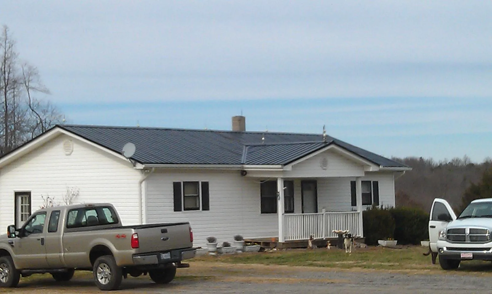 Finished dark metal roof on a white ranch home with work trucks parked in East Orange
