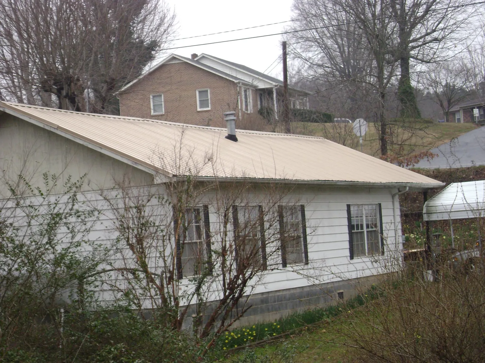 Tan metal roof on a white sided house set into a hillside — Commercial Roofing by Roofing Brothers in East Orange